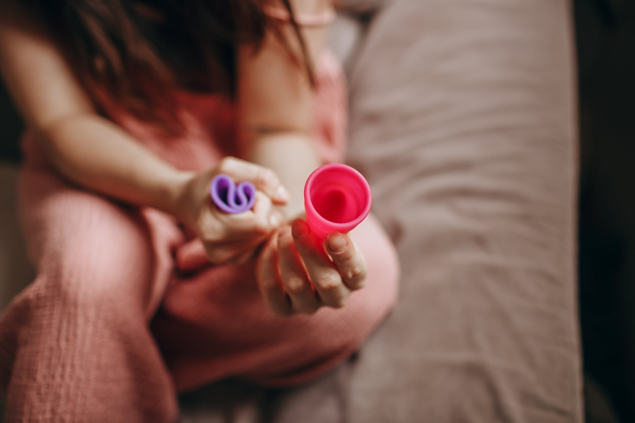 Woman sitting on bed holding a menstrual cup.