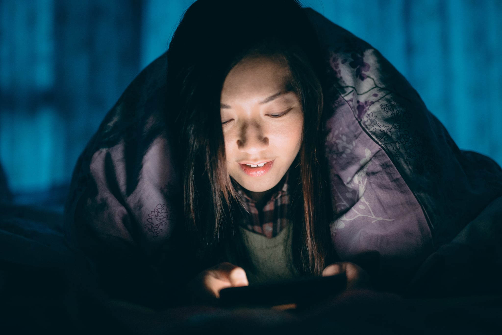 年轻女性智能手机下的床单在床上发短信。