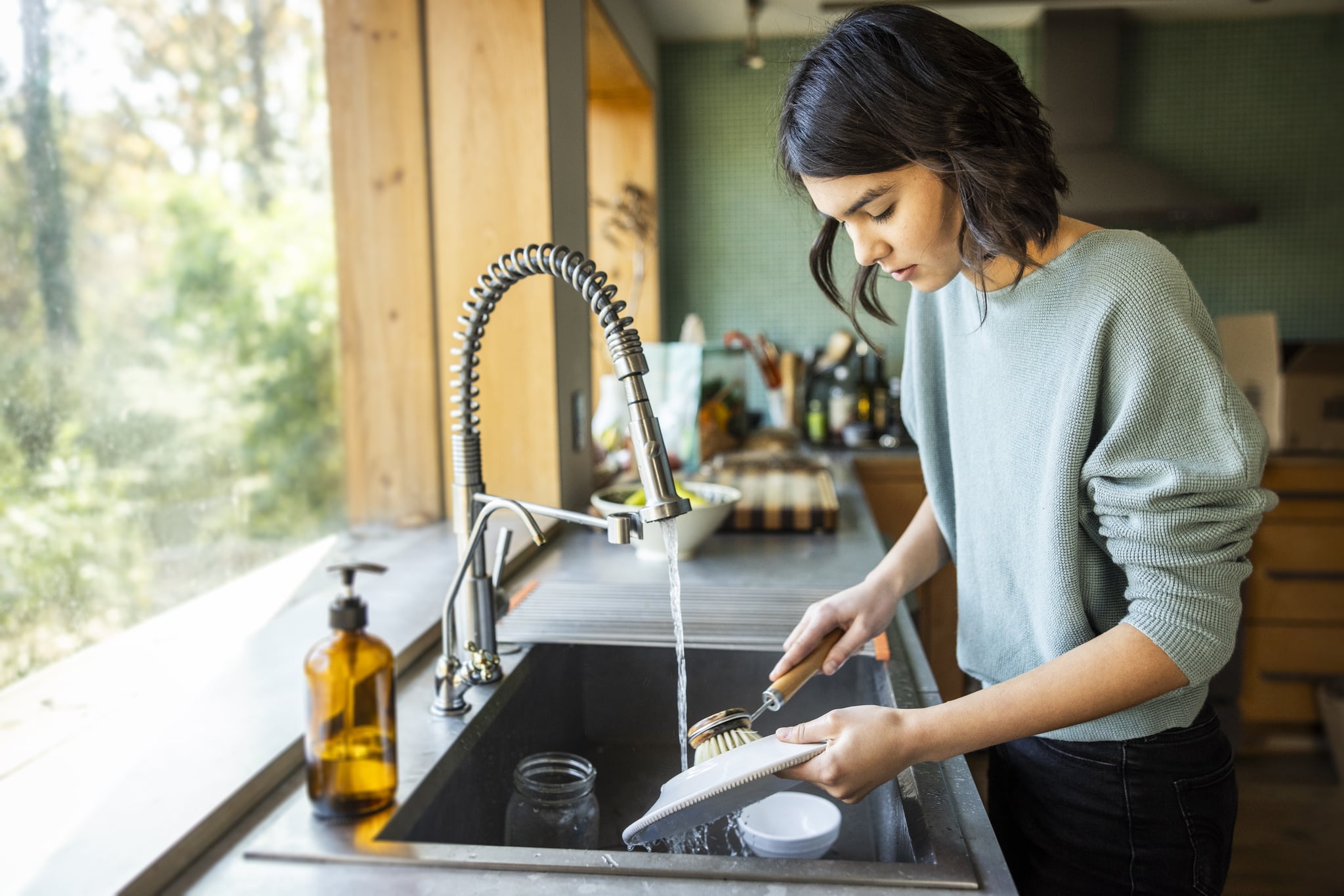 Teenage girl washing dishes in kitchen
