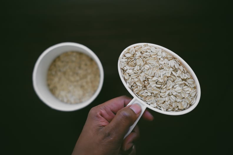 High angle view of unrecognizable black woman holding a measuring cup filled with old-fashioned rolled oats