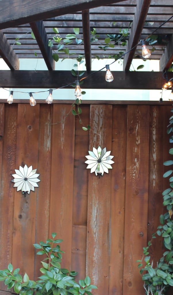 Tip #6: Hang Mirrors
Mirrors work just as well outdoors as they do indoors. They reflect surrounding greenery and light and can make a backyard space feel even bigger. These mirrored tea light sconces from World Market ($12) are perfect for adding a subtle glow to the walls after the sun sets. To create an even bigger illusion of space, try this DIY mirrored trellis! 
Tip #7: Know When to Play It Safe and When to Take Risks
An outdoor space is the perfect spot to take decorating risks. Layering vibrant accessories like rugs, accent tables, and umbrellas can create the same eye-catching impact as growing a colorful garden. Play it safe with key pieces, like furniture, but have fun with the rest!