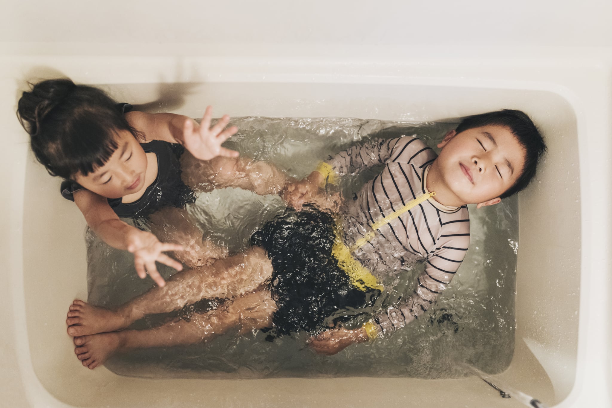 Asian brother and sister wearing swim wear and playing in the bathroom at home.