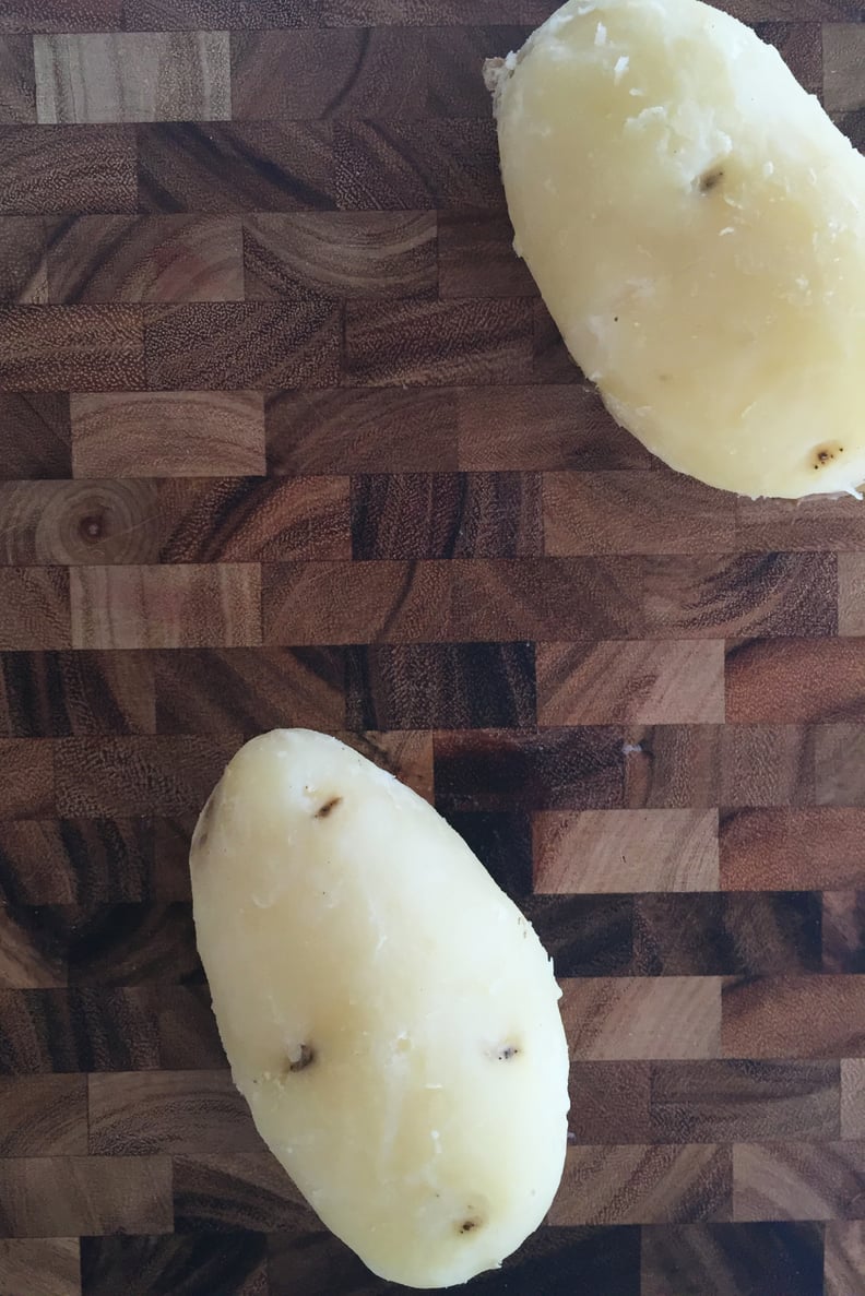 Two peeled potatoes on cutting board