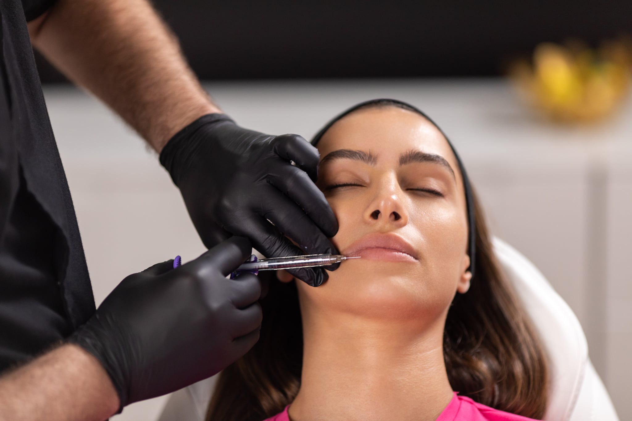Beautiful young woman receiving kind of aesthetic, beauty and health treatment. Male beautician holding syringe and injecting botox filler on her lips . She is beautiful and healthy