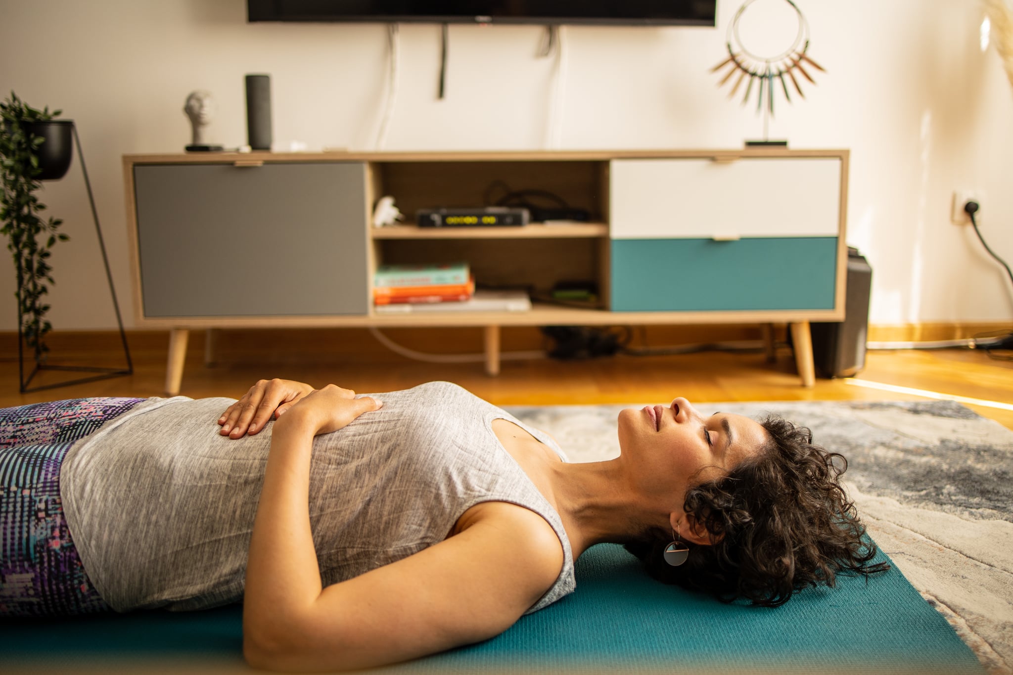 Side view of a Latin woman meditating on yoga mat at the living room. She is meditates with a video tutorial guide