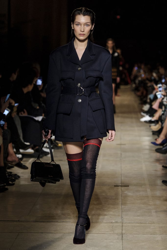 Bella walked down the Miu Miu runway in a structured jacket and sheer knee-high socks. Her look got a feminine touch from ankle-strap pumps, and she held onto a square belted satchel.