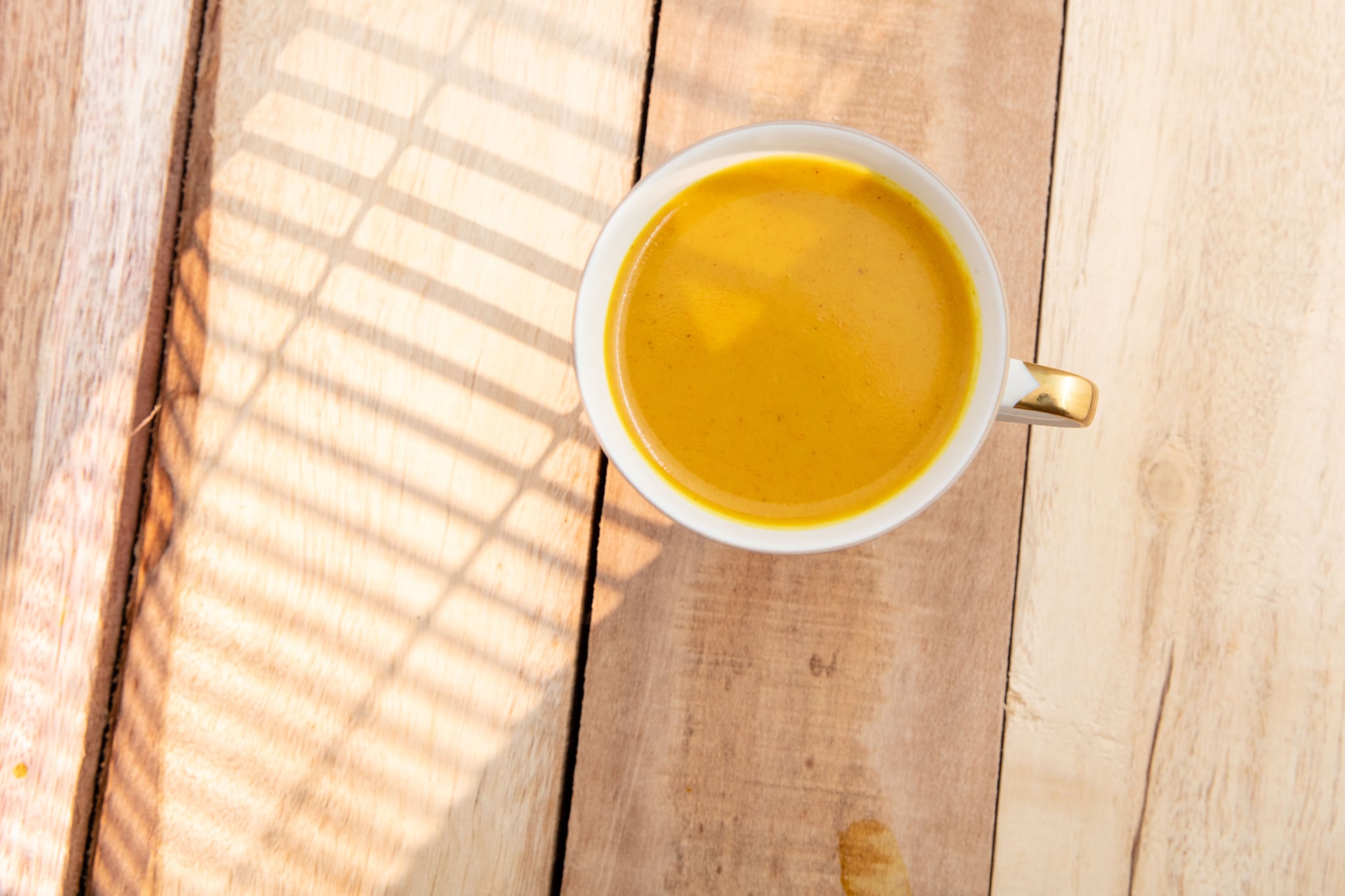 Hot turmeric latte. Served in white cup. Wooden plank. High point of view.