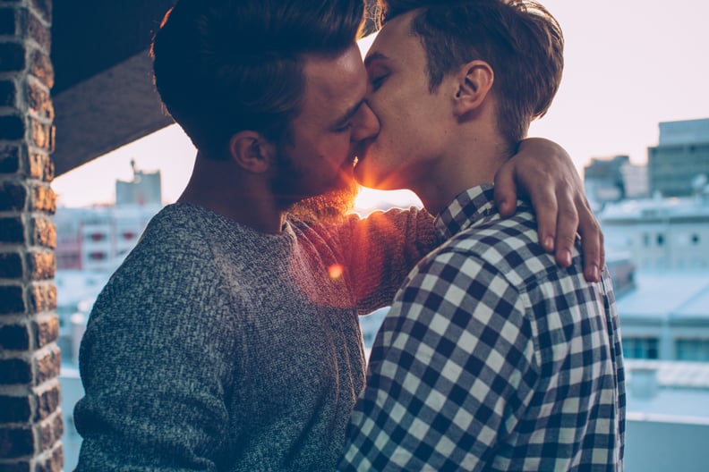 Young gay couple on the balcony enjoying in sunset. Wearing casual clothing. Kissing and embracing. Caucasian ethnicity, blond hair.