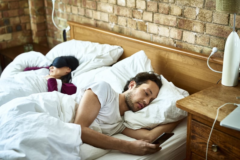 Mature man sending text message as his girlfriend sleeps in the bed, serious expression on face