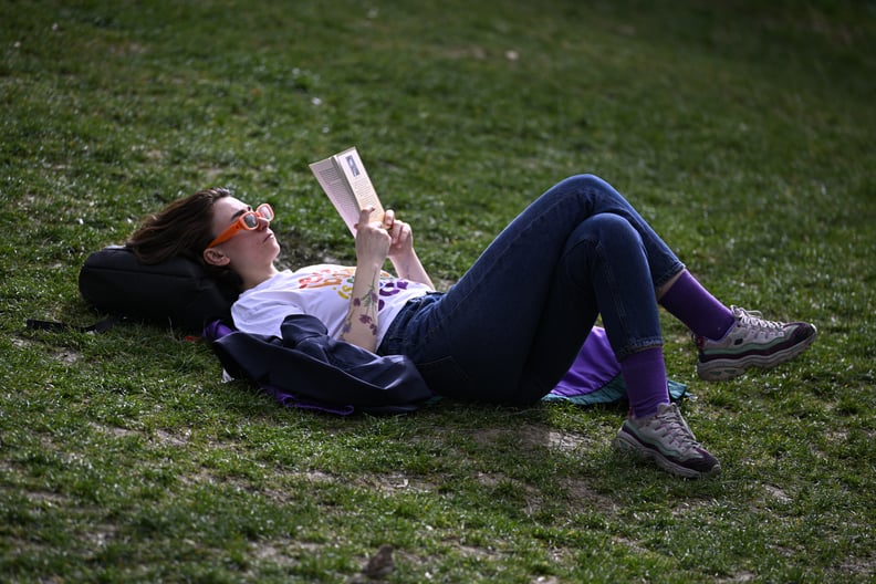 A woman in orange sunglasses and purple socks reads a book on green grass, remembering how to read more.