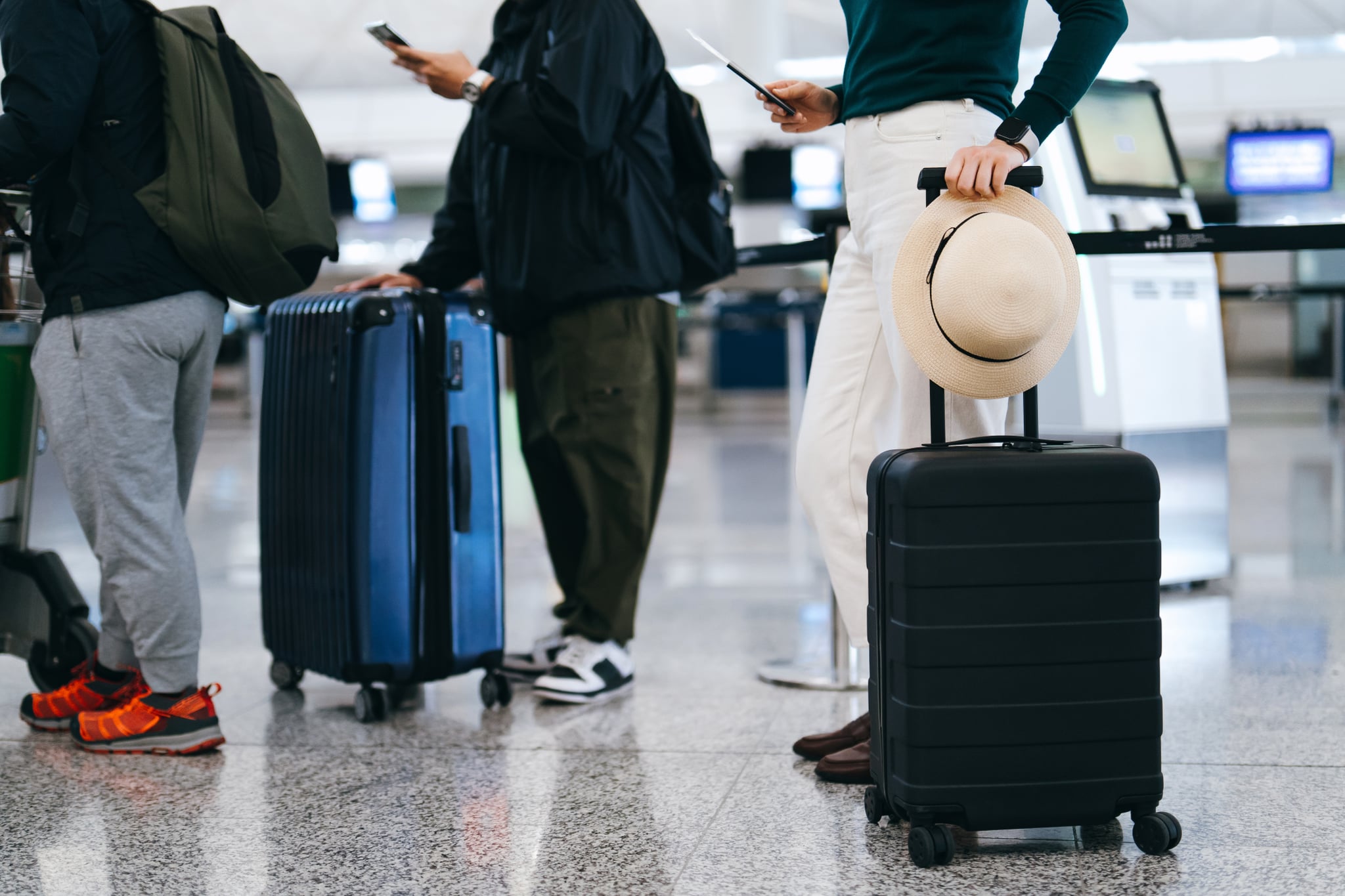 Cropped shot of group of airline passengers with suitcases standing in queue, waiting at check-in counter at International airport. 
