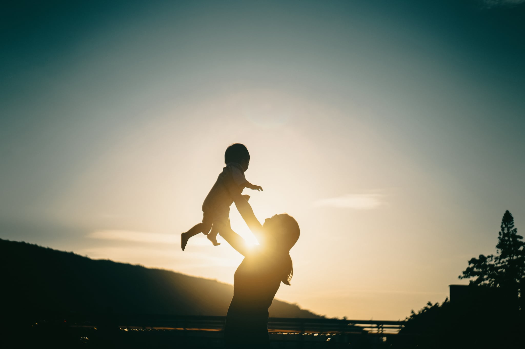 Silhouette of mother raising baby girl in the air outdoors against sky during a beautiful sunset