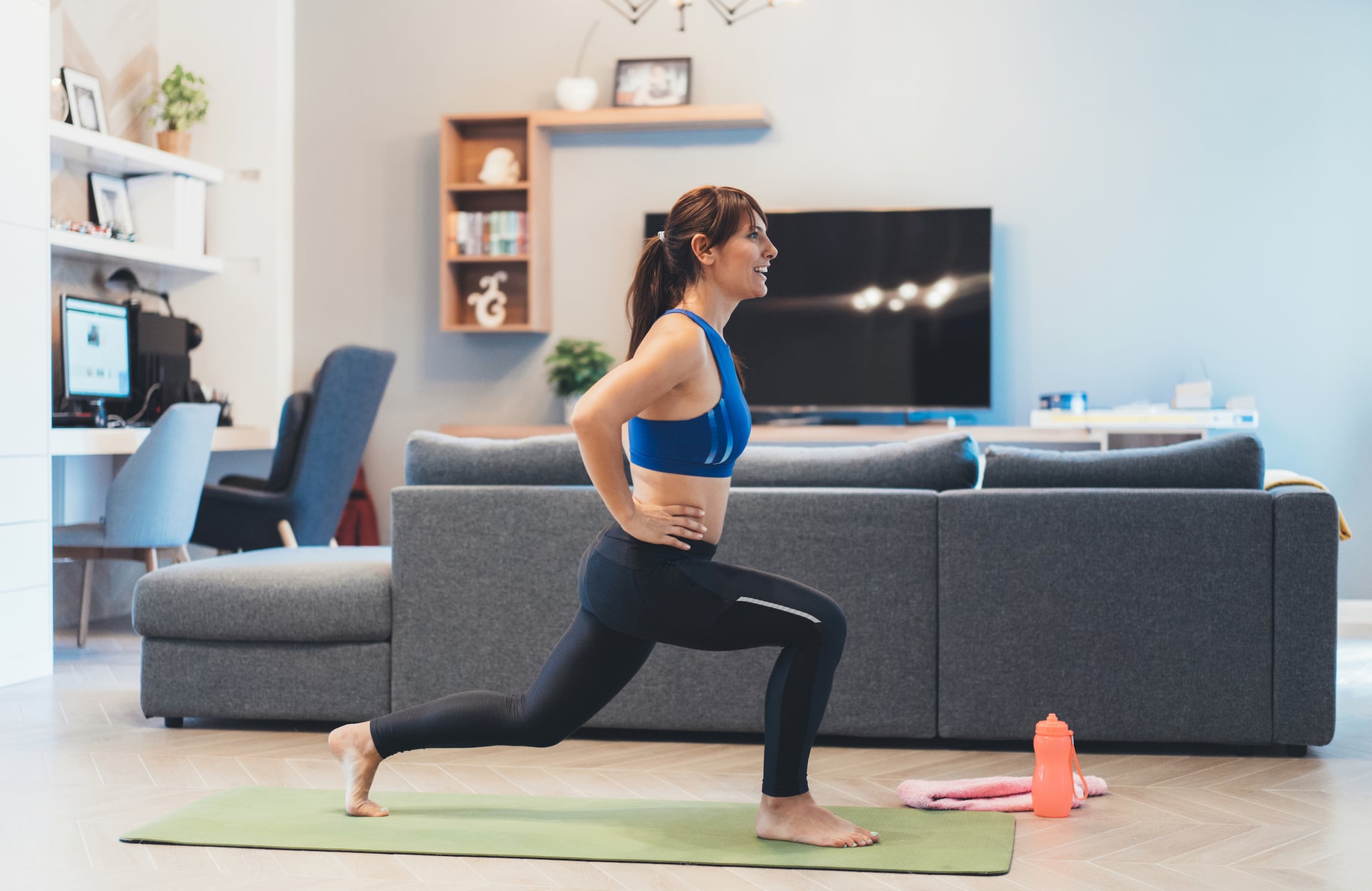 Fit woman doing frontal lunges indoors in a flat