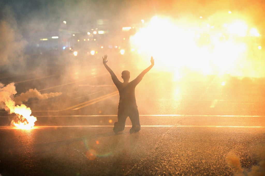 A women knelt in the streets with her hands up as tear gas filled the air. A women knelt in the streets with her hands up as tear gas filled the air.