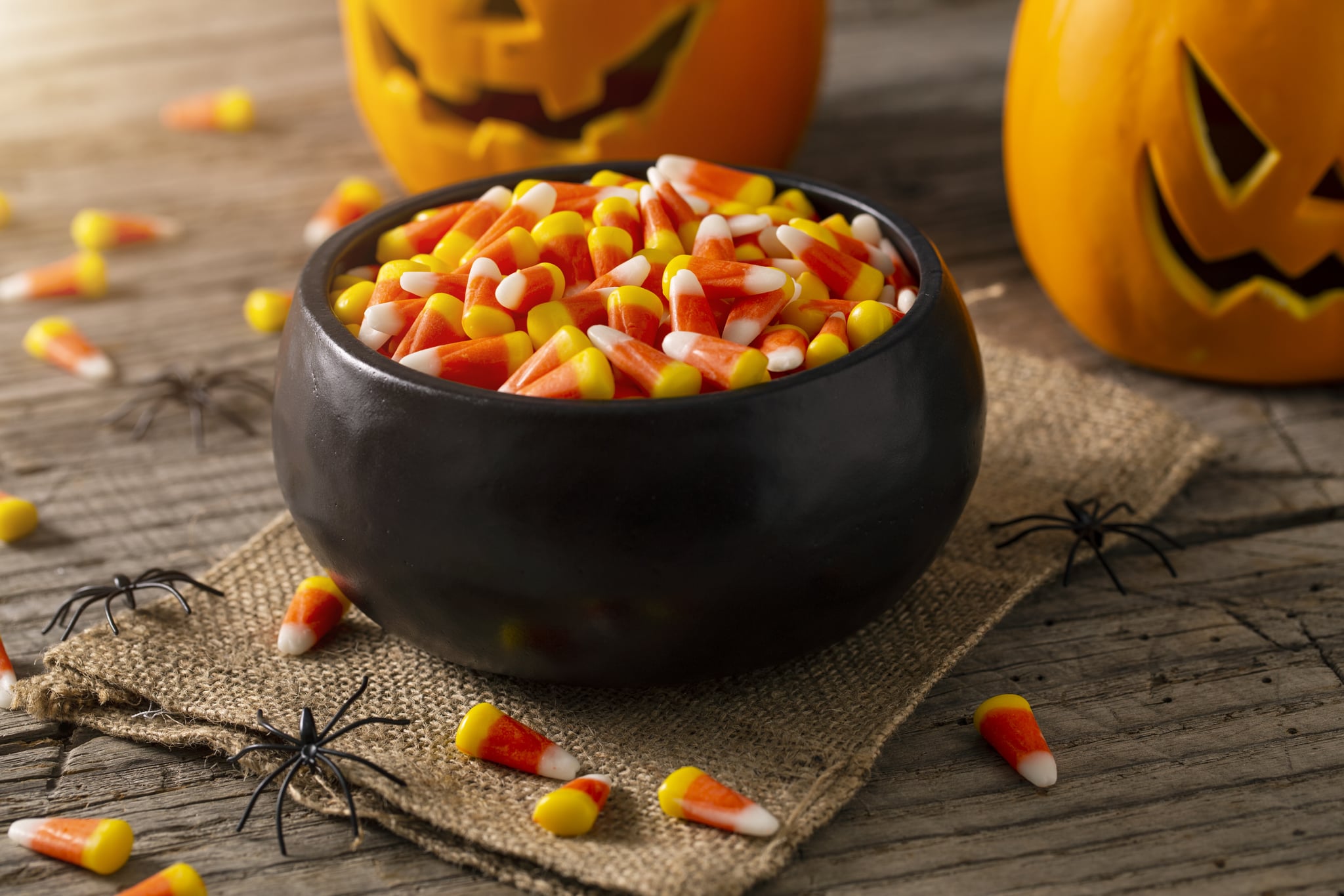 Bowl of Halloween candy corns with jack o' lanterns and spider decoration on rustic wood table.