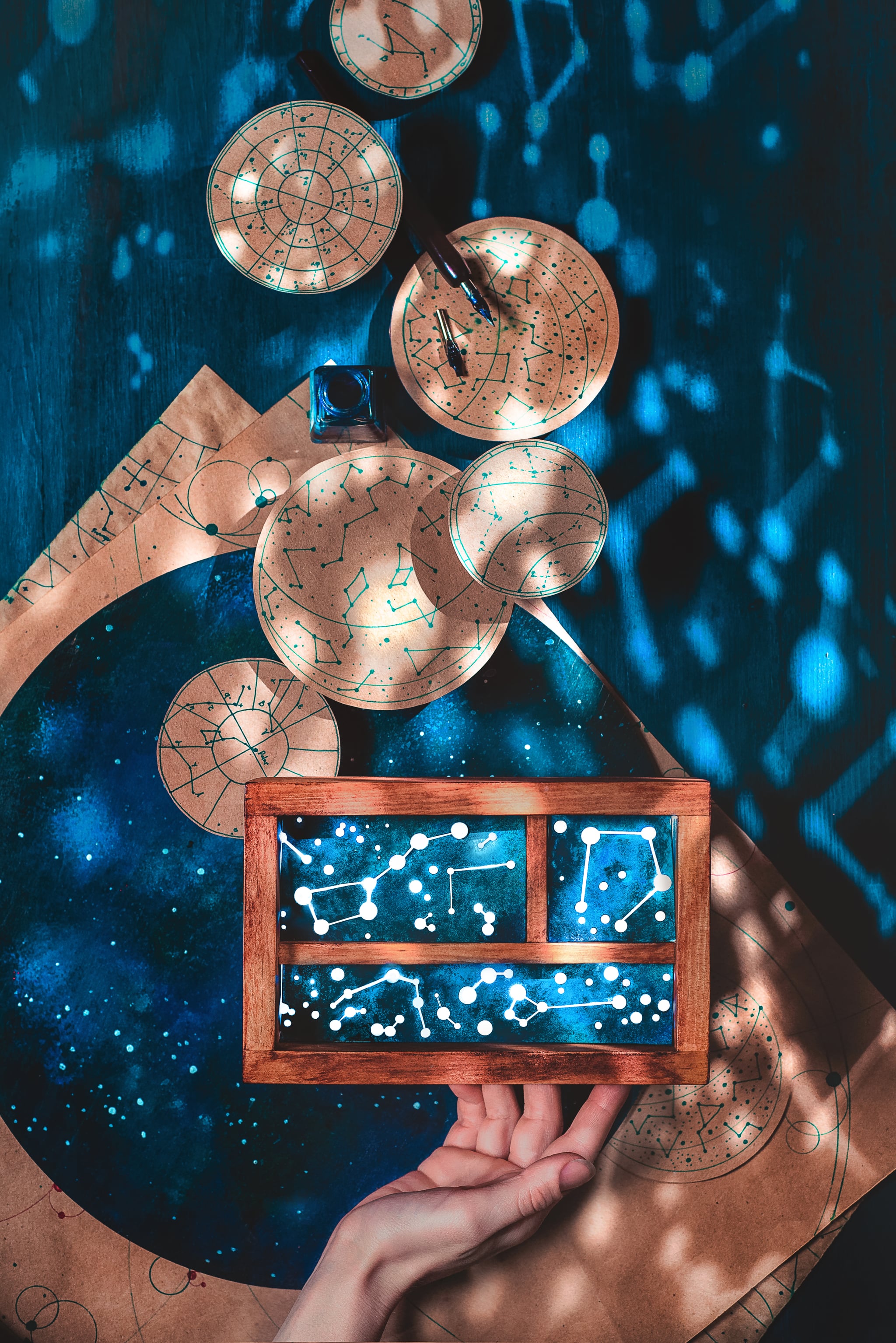 Hand touching handmade wooden box with glowing constellations inside. glares in form of constellations are covering the dark wooden background and notes with astronomical drawings.