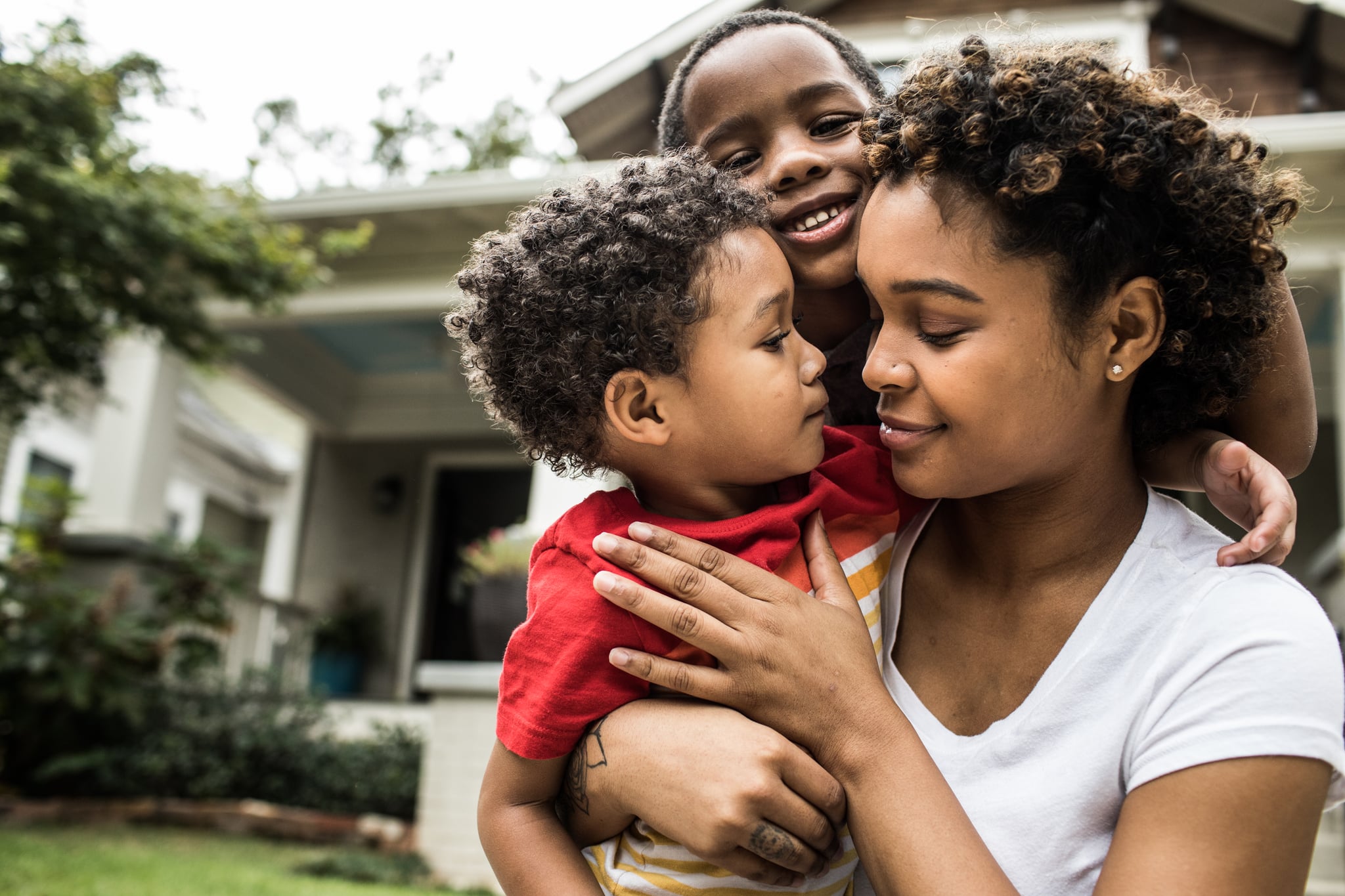 Single mother playing with young sons in front of house