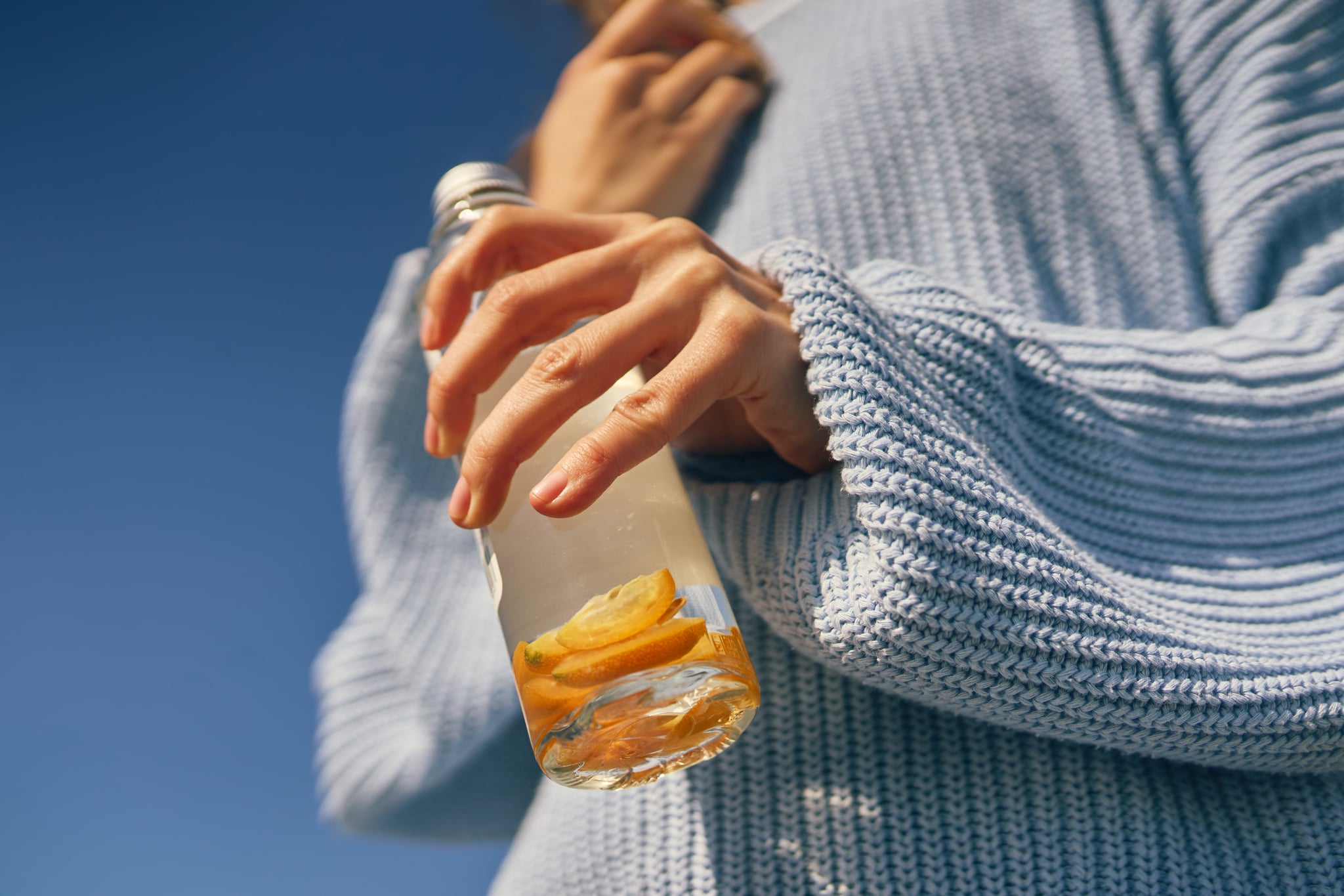 Woman holding a glass water bottle with lemon slices under a clear blue sky
