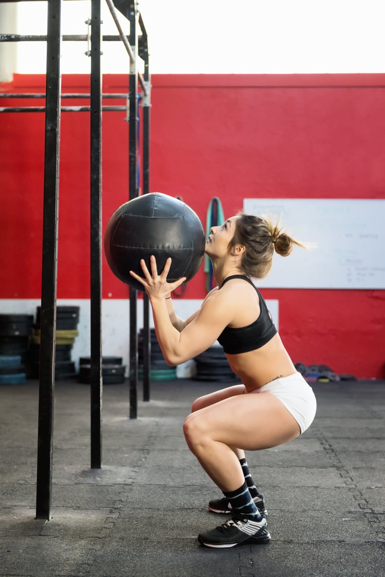 Vertical color profile view image of muscled woman training at gym with a medicine ball.