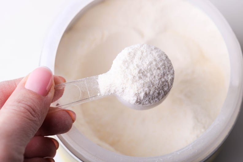 Close-up of white protein powder in jar with measuring spoon.
