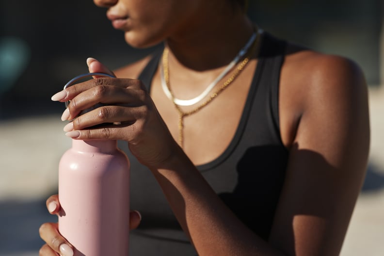Young woman opening pink water bottle on sunny day