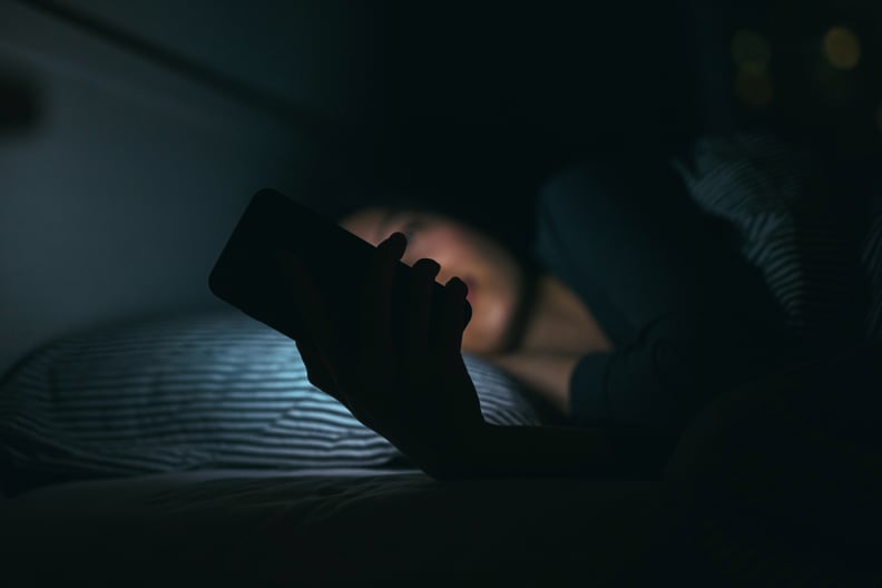 年轻女人短信智能手机而放松,晚上躺在床上