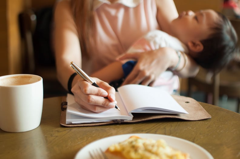 Working mom with her sleeping son on her arm while writing on a note pad