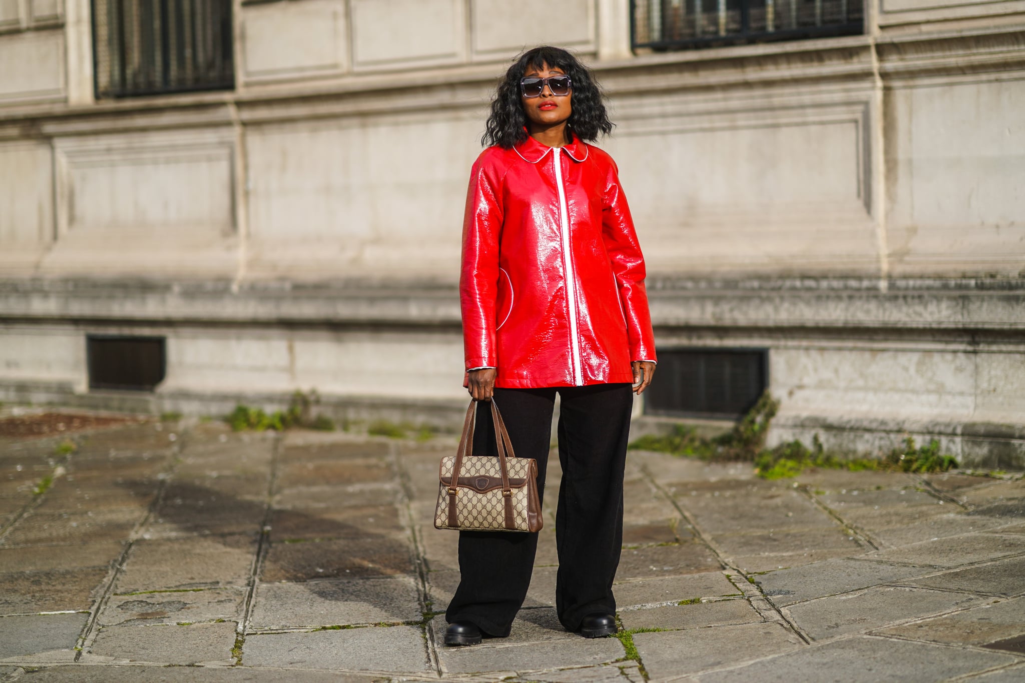 PARIS, FRANCE - FEBRUARY 20: Carrole Sagba aka Linaose wears sunglasses from Gigi Studio, a red shiny vinyl jacket, black flared pants from Bershka, black leather boots from Flattered, a brown Gucci monogram bag, on February 20, 2021 in Paris, France. (Photo by Edward Berthelot/Getty Images)