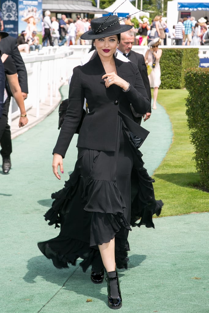 Opting for a monochrome look in a black ruffled dress, tailored blazer, and a hat.