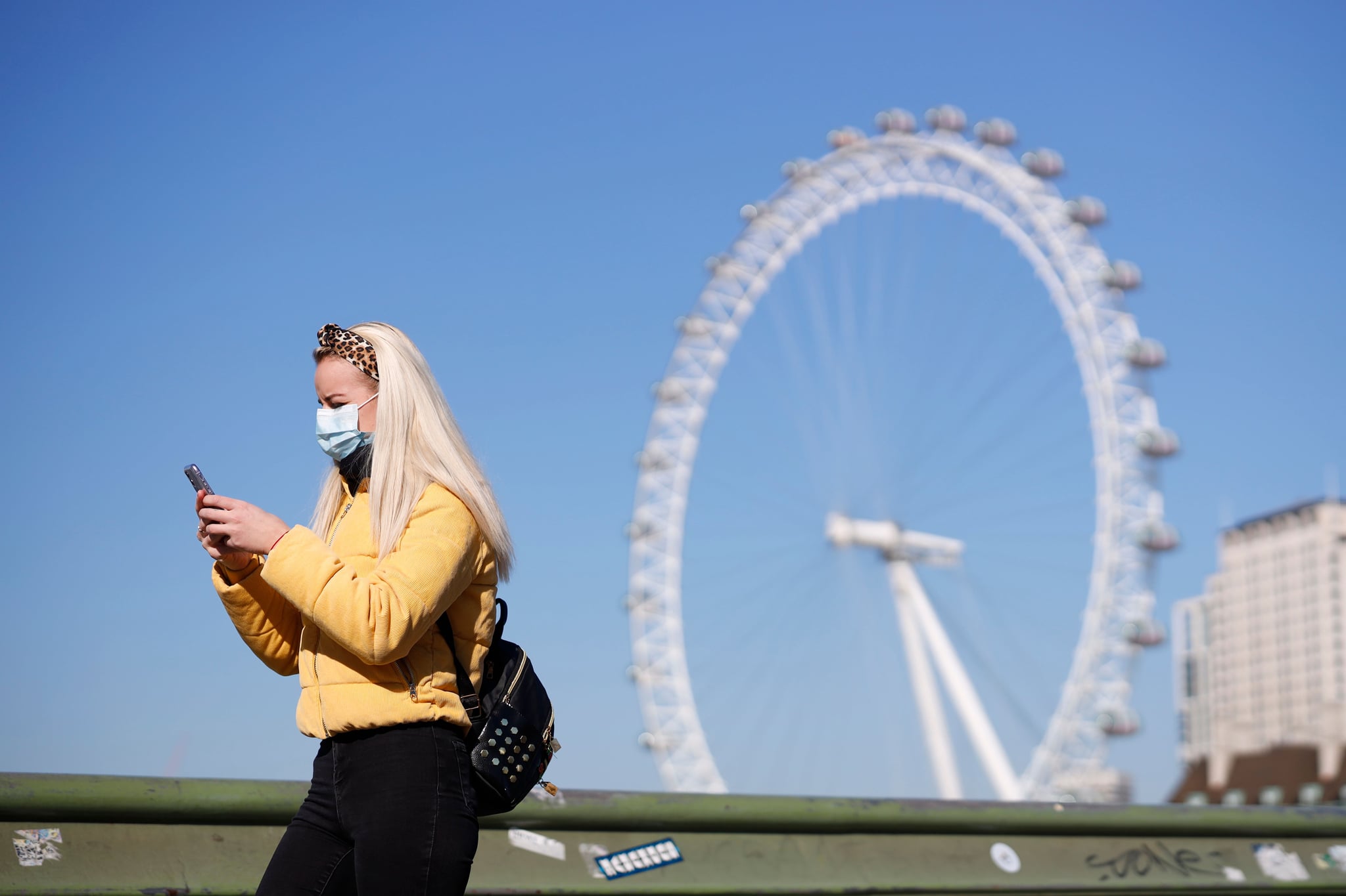 A pedestrian in a mask walks along Westminster Bridge with the London Eye in the backgroud, in a quiet central London on March 25, 2020, after Britain's government ordered a lockdown to slow the spread of the novel coronavirus. - Britain was under lockdown, its population joining around 1.7 billion people around the globe ordered to stay indoors to curb the 