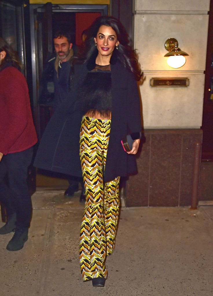 Amal paired her shimmering high-waist pants from Giambattista Valli's pre-Fall 2015 collection with a furry, bow-adorned crop top. The gold finish of her box clutch and her dangling earrings played up the yellow in her flares, and her chic black coat topped off her look.