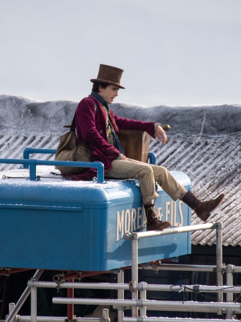 Timothée's beige striped trousers are rolled to the calves to show off some worn-in lace-up boots. Also, in this take, he's subbed in a simple navy scarf in lieu of the previous patterned one.