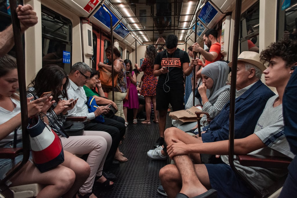  Crowded train car with diverse passengers sitting and standing, many using smart phones.