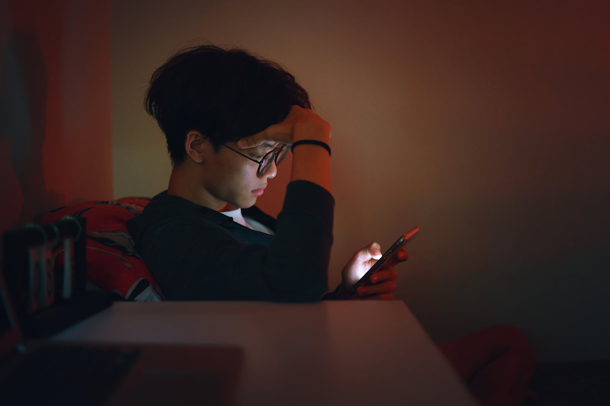 An upset teenage boy is reading alone on his smartphone late at night, caught in the grips of adolescent social media addiction.
