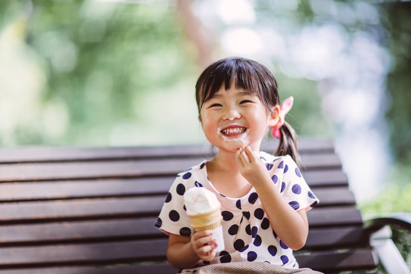 Lovely little girl sitting on the bench having ice-cream cone  in the park joyfully.