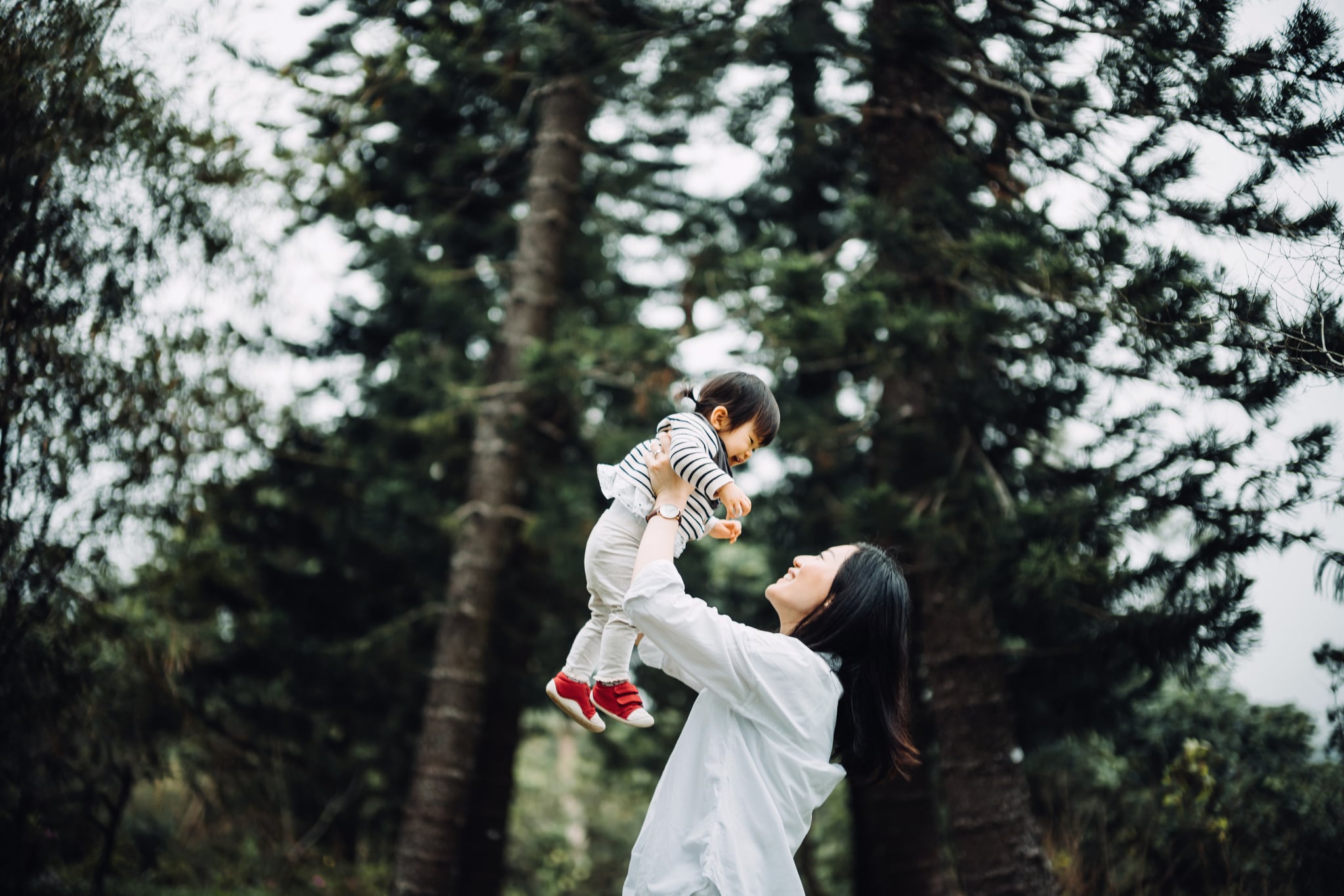 Joyful mother enjoying happy family time with cute toddler girl and lifting her in the air in nature park