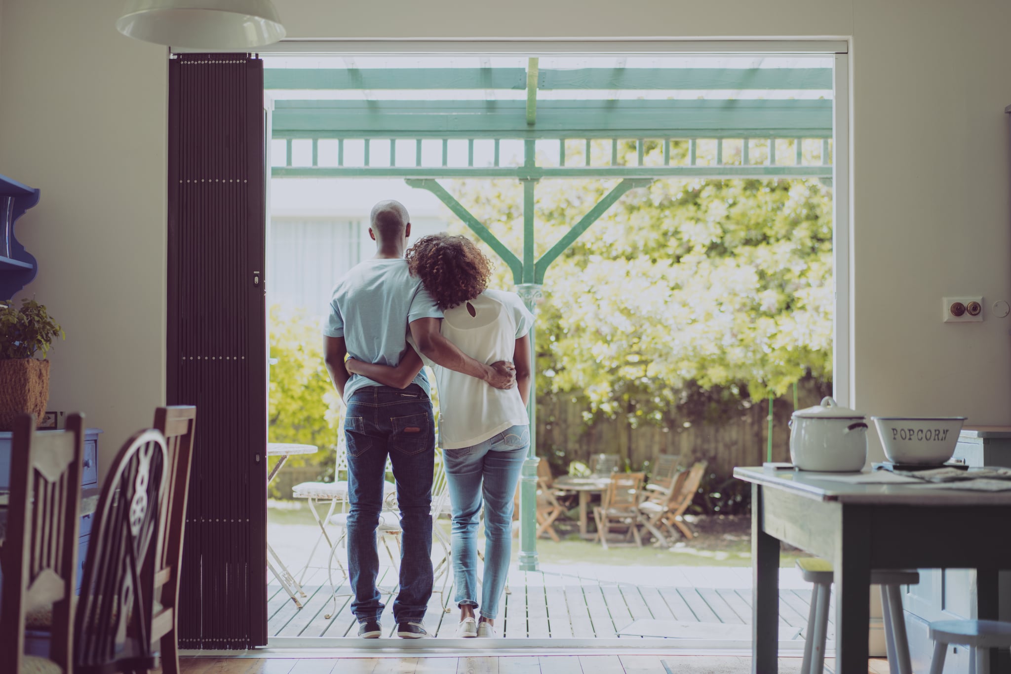 A photo of young couple standing arms around at entrance. Full length rear view of couple are in casuals. Satisfied loving man and woman spending quality time together at home.