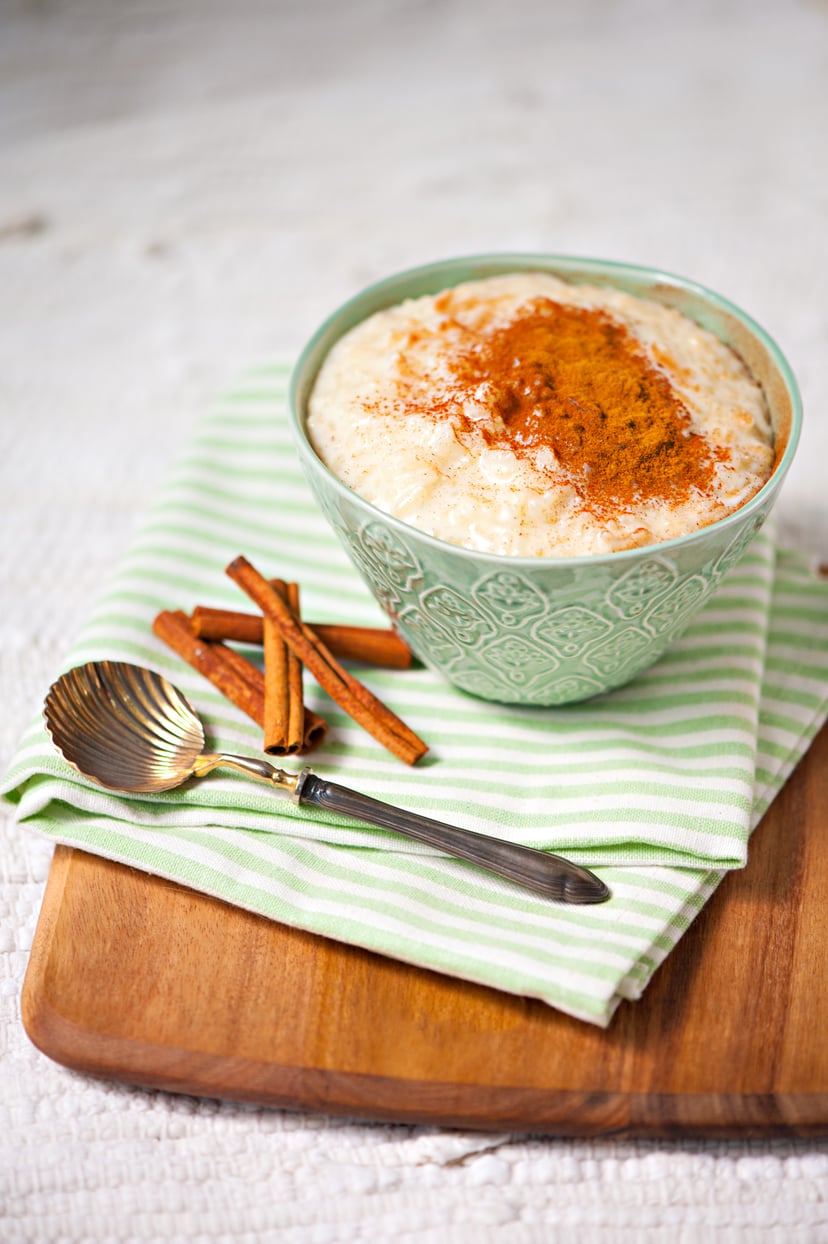 Milk rice pudding in green porcelain bowl with cinnamon powder on top, on a wooden board as background