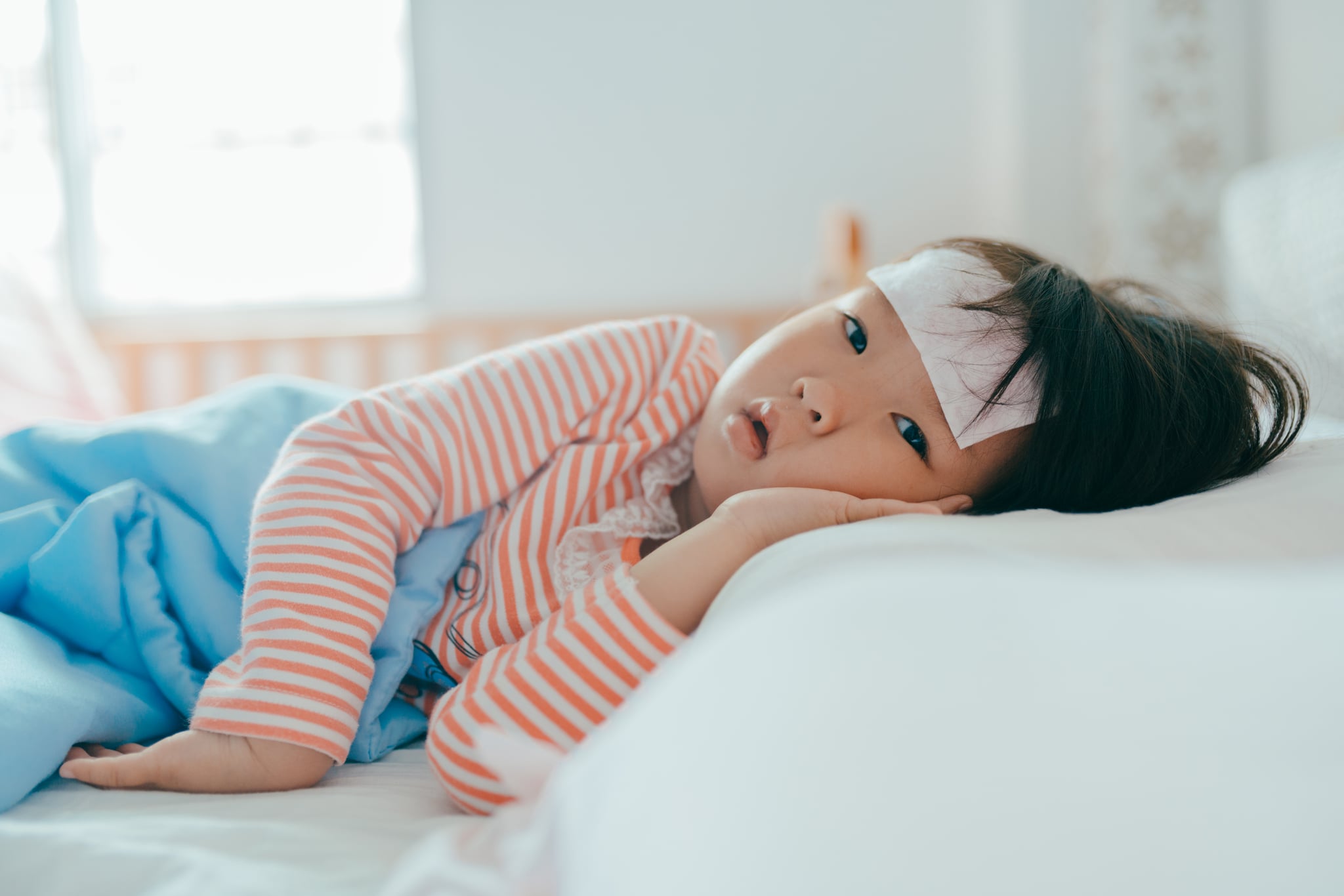 Asian sick little girl lying in bed with a high fever