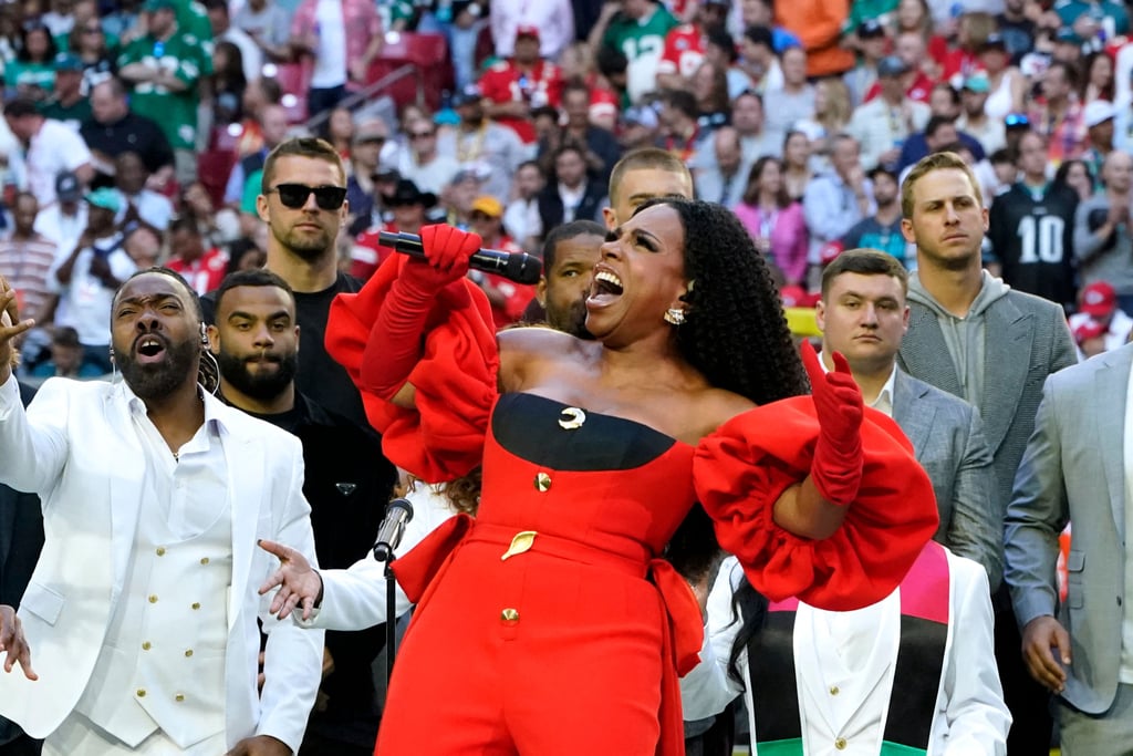 Sheryl Lee Ralph was red hot in a fiery power suit during her uplifting Super Bowl performance. The actor and singer gave a soulful rendition of "Lift Every Voice and Sing," wearing an outfit as bold as her voice. Ahead of the big game on Feb. 12, she wore a custom red Harbison jumpsuit tailored to absolute perfection. The look came complete with a dramatic train that pooled around her on a white platform and voluminous off-the-shoulder puff sleeves. Black fabric lined the back of the pantsuit and ran across her neckline, adding contrast to the shining gold hardware that trailed down her torso, featuring a delicate hammered gold leaf in the very center. 
As it turns out, good style runs in her family, with Ralph's 28-year-old daughter, Ivy-Victoria Maurice, serving as her stylist for the night. She accessorized her mom with elegant red gloves that reached her elbows, earrings by Nikos Koulis, and coordinating red open-toe pumps. Ralph left her hair down and kept her makeup simple yet stunning, with a smoky eye and neutral glossy lip. Behind her, several backup singers harmonized in monochromatic white suits, which emphasized Ralph's own bright color palette.
Ralph is one of many exciting performers at Super Bowl LVII, along with Rihanna, Babyface, and Chris Stapleton. Read on to get a closer look at her striking outfit, and stay tuned for more impressive game-day fashion moments ahead.
Related:
Rihanna Honors Her Son With "Mom" Ring at Super Bowl Press Conference