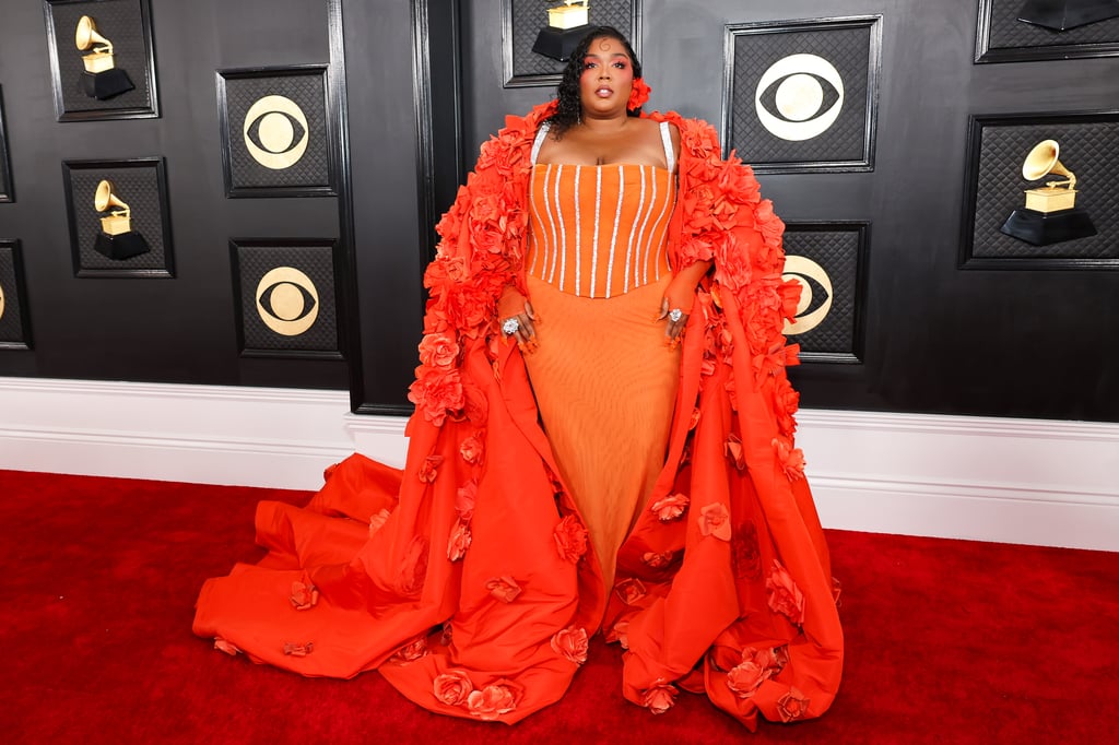 Lizzo proved more is more at the 2023 Grammys on Feb. 5. Accompanied by her boyfriend, Myke Wright, the singer strutted into the event in a dramatic cape dress hand-sewn with hundreds of silk flowers in vermillion. Her stylist, Patti Wilson, paired the custom ensemble with Swarovski statement rings and crystal-embellished mules.
Lizzo's floor-sweeping opera coat featured a hood adorned with even more delicate floral appliqués, bringing to mind a familiar chart-topping hit. "I can buy myself flowers," the singer captioned a red carpet photo of herself on Instagram, referencing Miley Cyrus's "Flowers." In another Instagram post, Lizzo wrote, "Spring awakening."
Beneath the avant-garde silhouette, Lizzo, who is nominated for five Grammy awards, wore a tangerine maxi dress with a silk corset bodice. The corset featured gleaming pinstripes and matching straps that beautifully complemented her extravagant jewelry. Bringing the look full circle, Lizzo wore sheer fingerless gloves and a vermillion flower in her hair. Accompanying Lizzo, Wright complemented the "Special" singer's outfit in a three-piece suit, a white button-up, and a black bow tie.
Her glam team — including Alexx Mayo, Shelby Swain, and Eri Ishizu — added extra splashes of color with sunset orange eyeshadow and a 3-D neon rose manicure. 
Later in the evening, Lizzo performed a medley onstage while wearing a black minidress with oversized puff sleeves and a shimmering corset design. She styled the look with glittering silver boots and a cross necklace.
See Lizzo's ensemble on the Grammys red carpet ahead.

    Related:

            
            
                                    
                            

            Lizzo Celebrates Valentine&apos;s Day Early in a Shimmery Thong and Matching Bra
