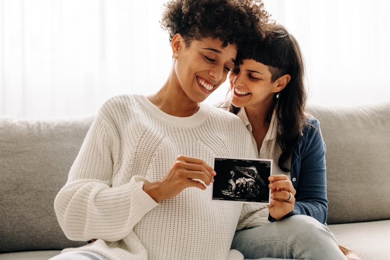 同性怀孕的夫妇拿着超声波扫描。准女同性恋夫妇微笑欣然而持有超声波检查胎儿的照片。年轻的同性恋情侣。