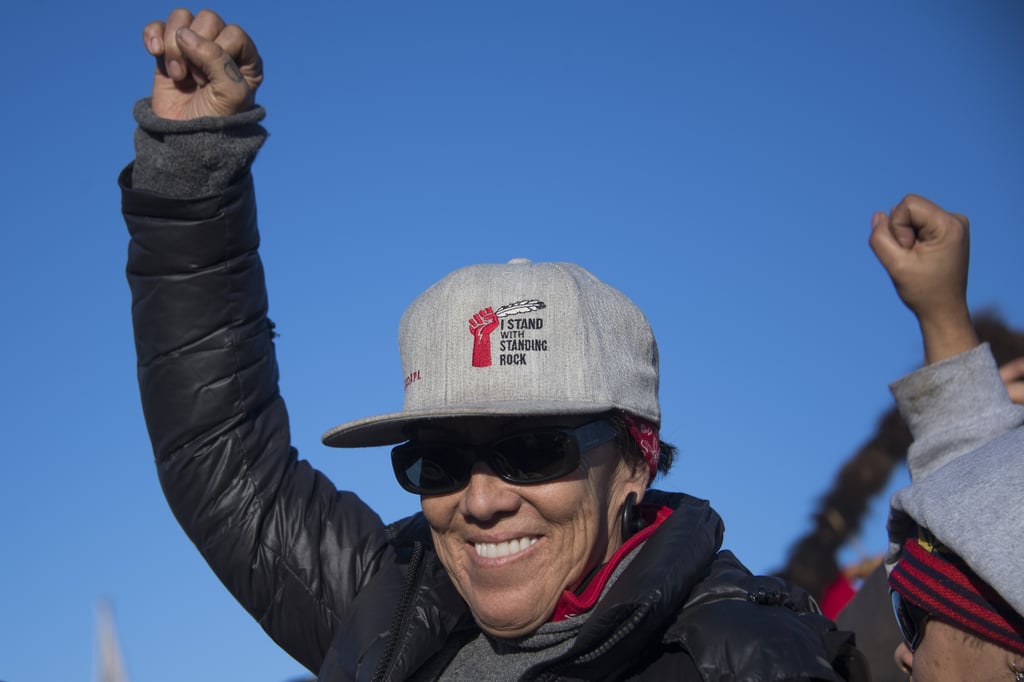 Another activist wearing a "I Stand With Standing Rock" hat raises a fist in the air.