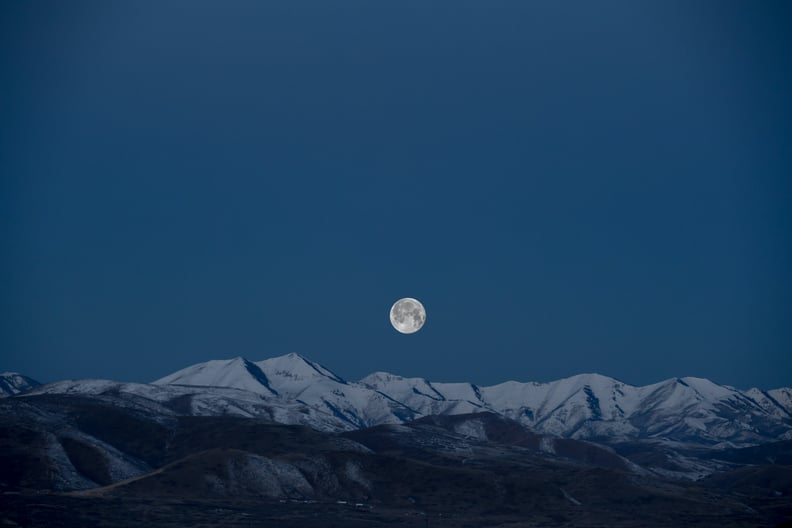 image of February full snow moon in starry sky over mountain peaks
