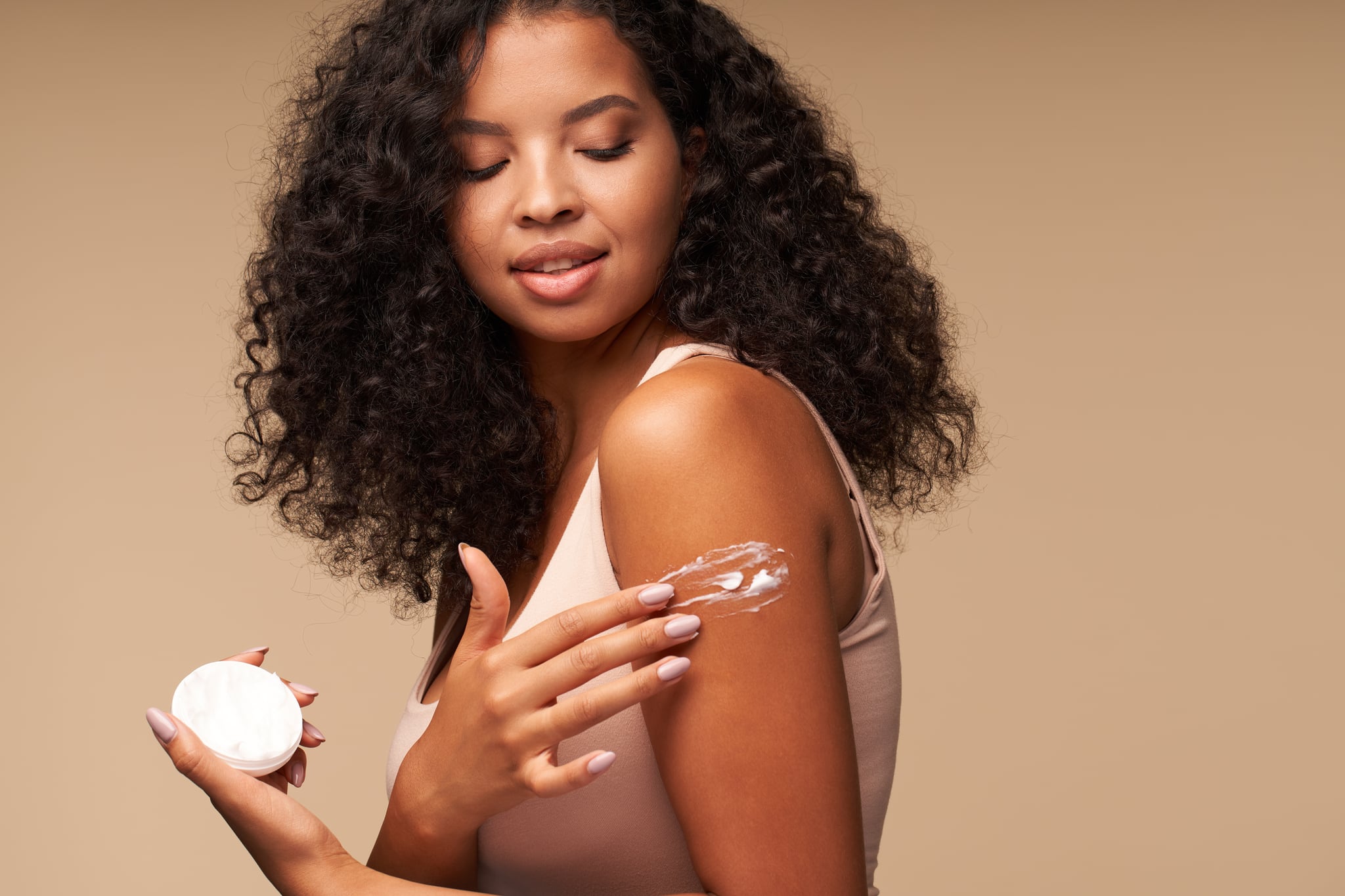 Woman applying cream on shoulder while standing against brown background