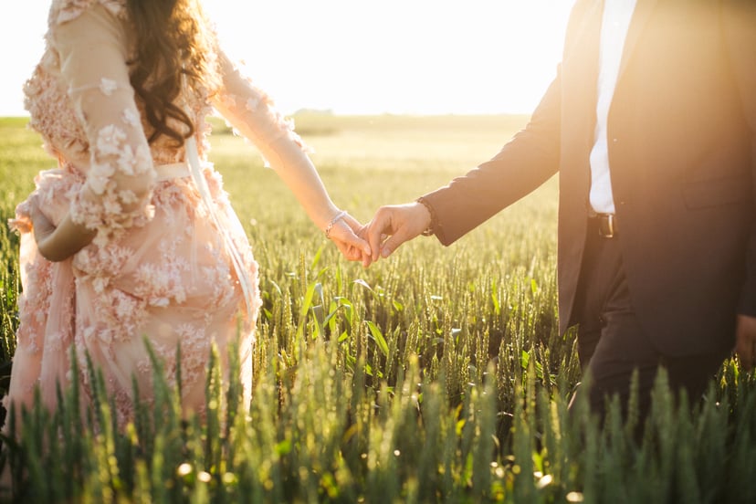 Bride holding grooms hand in field full of wheat