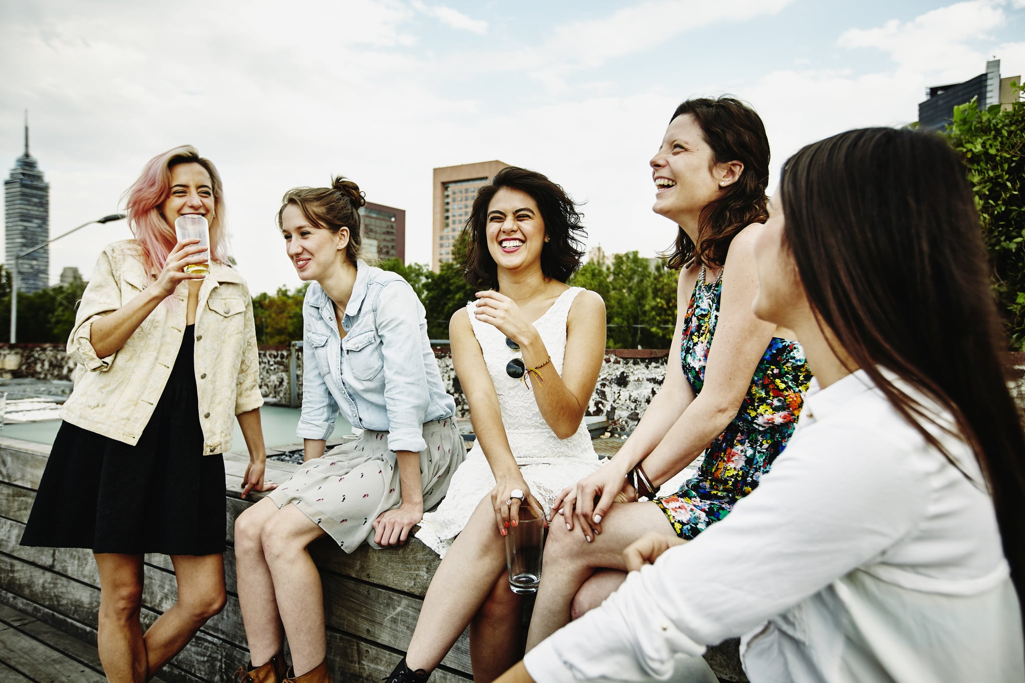 Laughing group of female friends having drinks together on rooftop deck