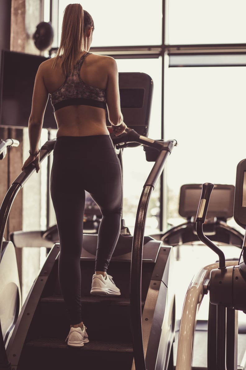 Rear view of fit young woman doing a light warm upon a stair climbing machine before her work out at the gym.