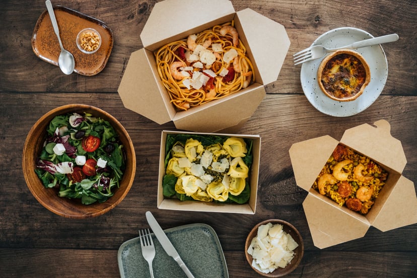 Flat lay view of delicious takeaway meals on dinner table - with pasta, vegetable salad and seafood risotto.