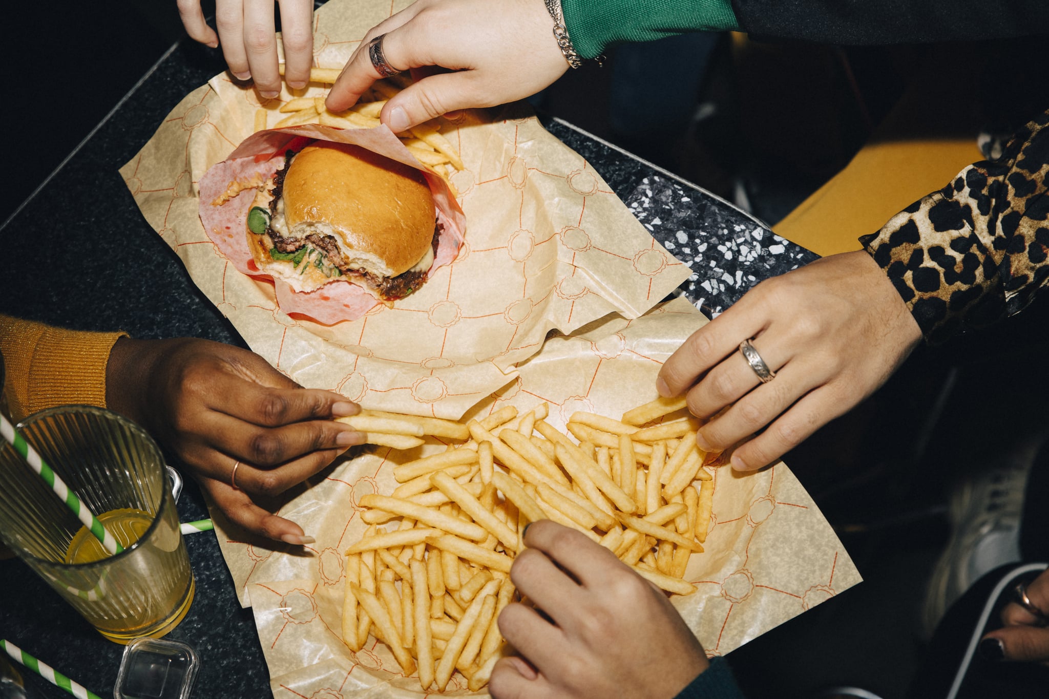 People reaching in to eat fries from a basket.